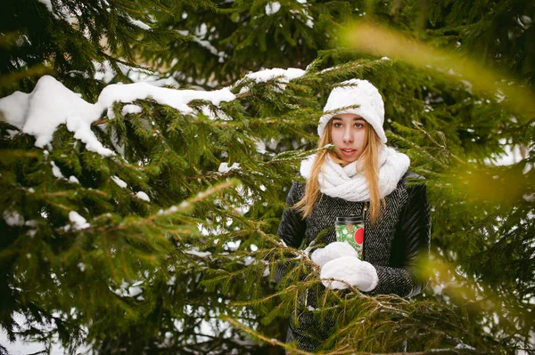 Porträt einer netten Frau in weißem Schal und Strickmütze auf Schnee und verwischten Tannenzweigen im Winter. — Stockfoto