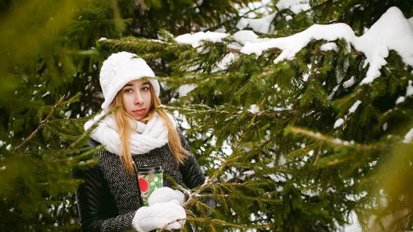 Porträtt av söt kvinna i vit halsduk och mössa stickad kappa på utomhus bakgrund av snö och suddig fir grenar på vintern — Stockfoto