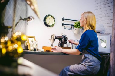 terzi dikiş makinesi çalışmalarına. Genç sarışın kadın evde mekanik bir dikiş makinesinde çalışma masanızın başında oturan dikmek için hazır olun