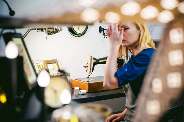 Trabajo de costurera en la máquina de coser. joven mujer rubia trabajando en una máquina de coser mecánica en casa sentado en su escritorio, estar preparado para coser — Foto de Stock