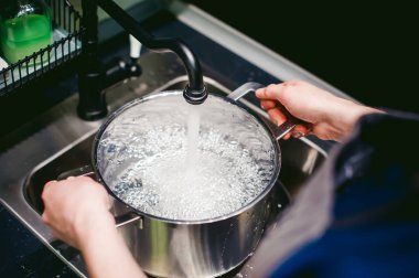 kadın ev kadını mutfakta. Kız tavada musluktan su toplar