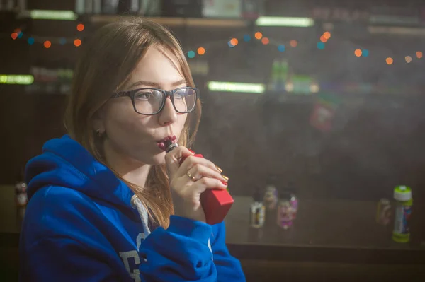 Όμορφη νεαρή γυναίκα με γυαλιά που καπνίζει ηλεκτρονικό τσιγάρο — Φωτογραφία Αρχείου