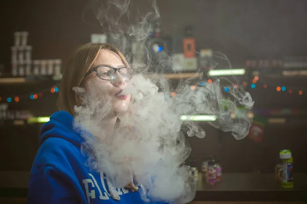 Όμορφη νεαρή γυναίκα με γυαλιά που καπνίζει ηλεκτρονικό τσιγάρο — Φωτογραφία Αρχείου