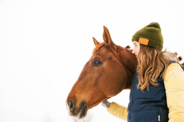 At ve kadın kış giysileri içinde birlikte karşı beyaz kar bekletin. sevgi ve atlar için bakım. Beyaz bir arka plan üzerinde hayvan portre.