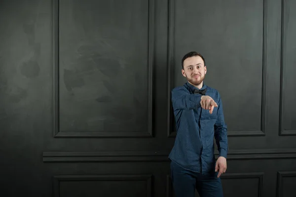 Retrato de estudio de un joven hipster sobre un fondo de pared oscuro con una camisa azul y jeans . — Foto de Stock