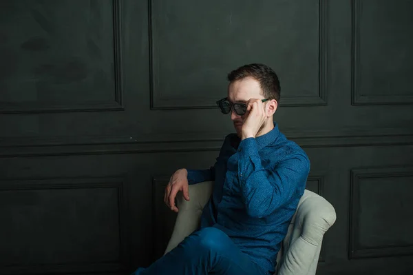 Studio πορτραίτο ενός άνδρα νέοι hipster σε ένα φόντο σκούρο τοίχο σε ένα μπλε πουκάμισο και τζιν. — Φωτογραφία Αρχείου