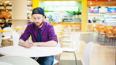 portre genç adam bir ekose gömlek ve kravat ve bir kap içinde sakallı oturur bir sandalye bir masa gıda mahkeme alışveriş merkezinde