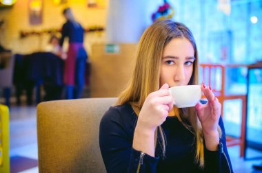 bir fincan elinde tutan bir siyah elbiseli genç kadın