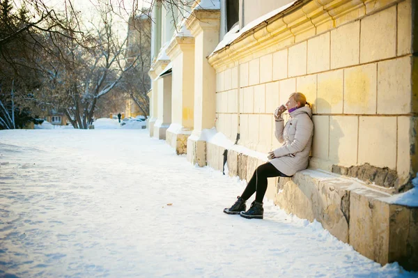 Jonge vrouw gekleed in warme kleren afhaalmaaltijden koffie drinken uit de beker op straat in de winter — Stockfoto