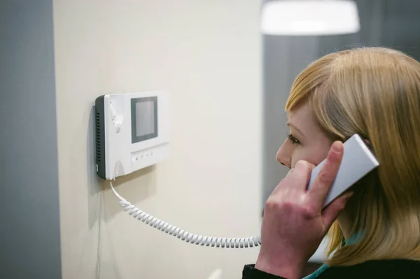 Blonde vrouw beantwoordt de oproep van de intercom terwijl de telefoon aan uw oor — Stockfoto