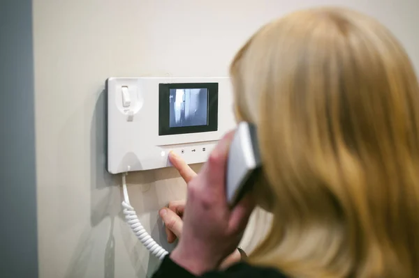 Wanita pirang menjawab panggilan interkom sambil memegang telepon ke telinga Anda Stok Foto