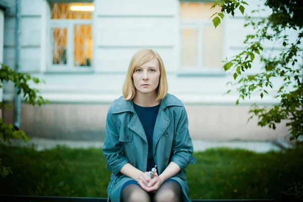 Outdoor Portret van de jonge blonde vrouw, het dragen van een regenjas, elektronische sigaret roken — Stockfoto