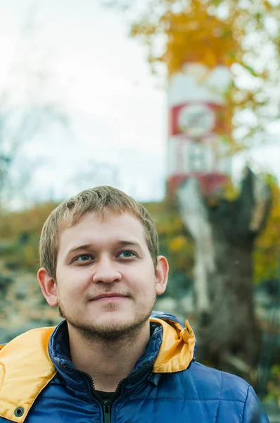 Retrato de un hombre en una chaqueta sobre un fondo de un faro en el otoño — Foto de Stock