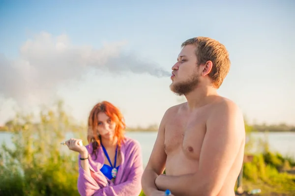 Молода пара відпочиває на пляжі, курить електронну сигарету — стокове фото