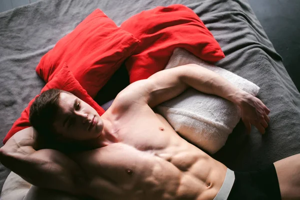 Studio portret jonge sexy mannen bodybuilder atleet, met een naakte torso, ligt op een bed in kussens in ondergoed — Stockfoto