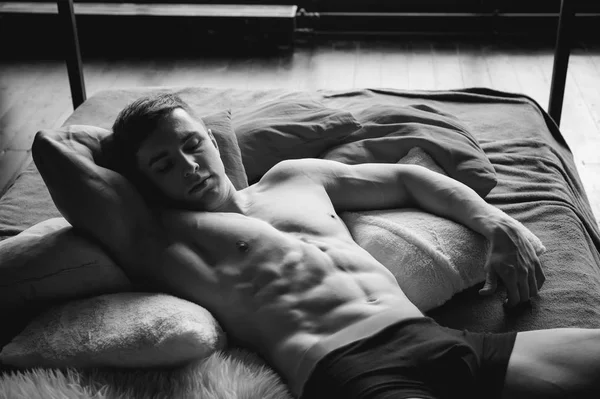 Potret studio laki-laki muda seksi binaragawan atlet, dengan tubuh telanjang, terletak di tempat tidur di bantal di pakaian Stok Gambar Bebas Royalti
