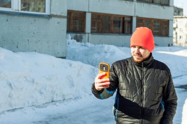 Adam kendini fotoğraf çekme. bir sonbahar spor rahat ceket ve parlak turuncu şapka giymiş sakallı adam selfie telefon şık durumunda, açık havada güneşli kış gününde yürüyüş yapar