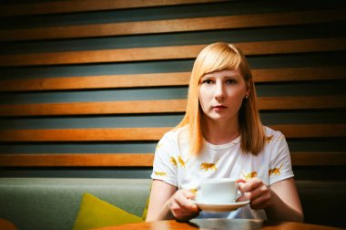 Sarışın genç kadın ile beyaz T-shirt giyen baskı, öğle yemeği zamanı Cafe ziyaret