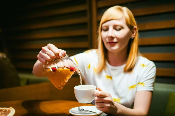 Mujer rubia joven con camiseta blanca con estampado, hora del almuerzo en la cafetería visitada —  Fotos de Stock