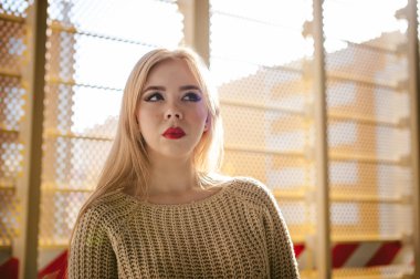 Örme kazak ve kot giymiş genç bir kadın portresi. Ayakta yakınındaki bir metal delikli Park çit İnşaat