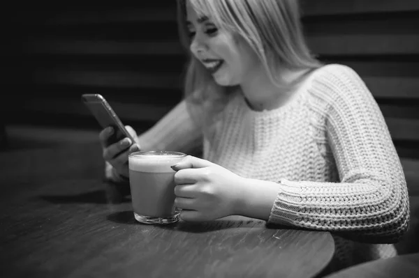 Giovane donna bionda in un maglione a maglia, fare una foto selfie su uno smartphone, seduta a un tavolo in un caffè, passare del tempo da sola, fare comunicazione su Internet — Foto Stock