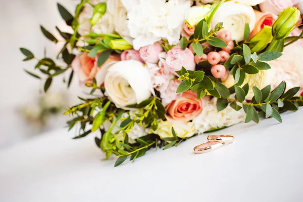 Fénykép kép-ból egy klasszikus Arany jegygyűrűt a menyasszony és a vőlegény, a fehér asztal, és egy gyönyörű menyasszonyi csokor virág a menyasszony — Stock Fotó