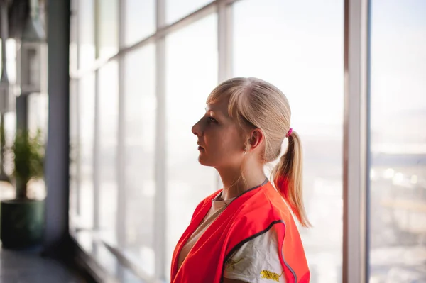 Portrait of a female employee in an orange robe vest in the working space of a production room, against a background of large windows — Stock Photo, Image