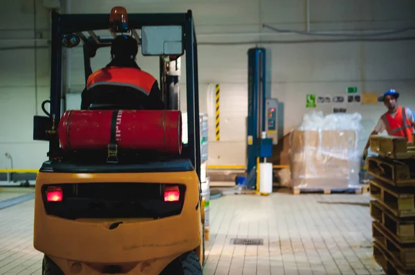 Warehouse employee in Overalls clothes, driver Reachtruck busy working on logistics Moving on loader pallets with beer kegs on line of factory for production of beer. human labor in manufacturing