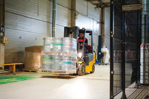 Karyawan gudang pakaian Overalls, sopir Reachtruck sibuk bekerja pada logistik Pindah pada palet pemuat dengan tong bir pada baris pabrik untuk produksi bir. tenaga kerja manusia dalam pembuatan Stok Foto