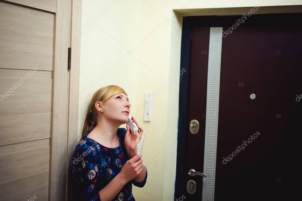 blonde woman answers the intercom call, hold the phone to his ear, waiting for the arrival of the long-awaited guest. Being in apartment near front door