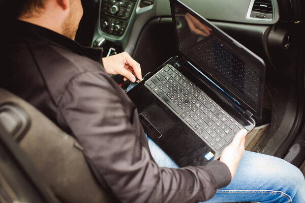 Человек с ноутбуком в машине тюнингует систему управления, обновляет программное обеспечение
