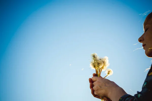 Young blonde girl in dress with shoulder bag, walking on dandelion field