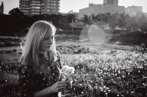 Молодая блондинка в платье с плечевой сумкой, ходит по одуванчику
