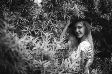 Siyah ve beyaz bir şapka çalıların arasında olan bir genç kadın portresi