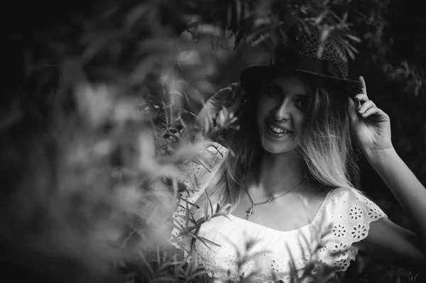 Black and white portrait of a young woman with a hat in bushes