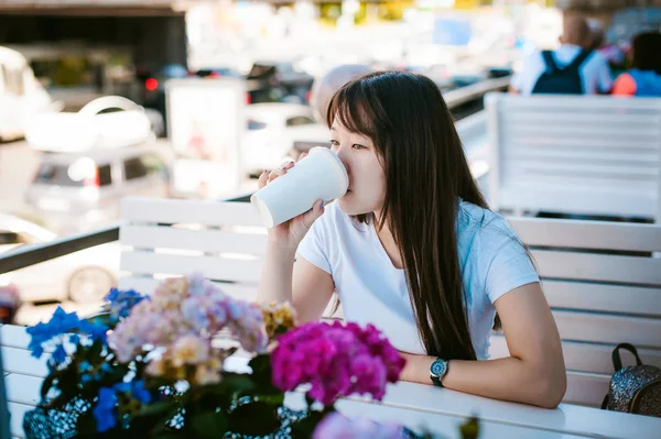 Linda mujer joven asiática en el café de verano al aire libre. chica en camiseta blanca, con el pelo largo en el interior acogedor luz simple del restaurante de estilo urbano —  Fotos de Stock