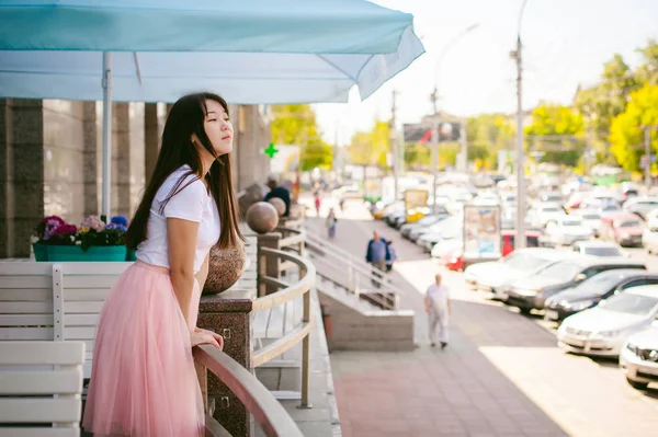 Roztomilý asijský mladá žena v letní kavárně venku. dívka v bílém tričku, s dlouhými vlasy v jednoduché lehké útulný interiér restaurace Urban stylu — Stock fotografie
