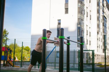 Güneşli sabah açık havada spor tesislerinde CrossFit egzersiz yapan yakışıklı seksi erkek vücut geliştirmeci atlet erkek. Sağlıklı yaşam konsepti. Vücudun fiziksel hazırlık. Kas gösterilen modeli pozlar