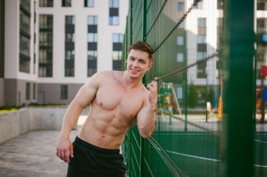 Yakışıklı seksi erkek vücut geliştirmeci sporcu adam çıplak gövde ile bir güçlü kas vücut ayakta gösterilen pozlar courtyard bir yeşil kılavuz çit spor alanında yakınındaki. Sağlıklı yaşam konsepti.
