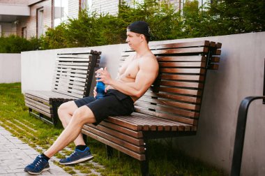 Çıplak gövde evin avlusunda bir bankta eğitim içecekler su bir şişe sonra bir erken güneşli yaz sabahı dinlenme adamla yakışıklı seksi erkek atlet