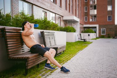 Çıplak gövde evin avlusunda bir bankta eğitim içecekler su bir şişe sonra bir erken güneşli yaz sabahı dinlenme adamla yakışıklı seksi erkek atlet