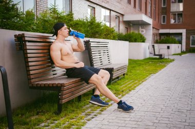 Çıplak gövde evin avlusunda bir bankta eğitim içecekler su bir şişe sonra bir erken güneşli yaz sabahı dinlenme adamla yakışıklı seksi erkek atlet