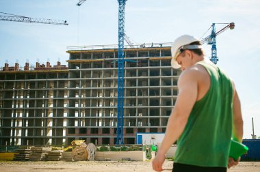 Genç seksi erkek vücut geliştirmeci atlet. Müdür mühendis Oluşturucu koruyucu kask yapı ve inşaat İnşaat arka plan üzerinde duran beyaz belgeleri ile el vinç