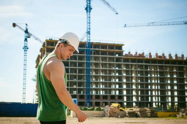 Genç seksi erkek vücut geliştirmeci atlet. Müdür mühendis Oluşturucu koruyucu kask yapı ve inşaat İnşaat arka plan üzerinde duran beyaz belgeleri ile el vinç