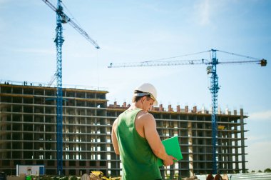 Genç seksi erkek vücut geliştirmeci atlet. Müdür mühendis Oluşturucu koruyucu kask yapı ve inşaat İnşaat arka plan üzerinde duran beyaz belgeleri ile el vinç