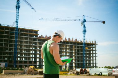 Genç seksi erkek vücut geliştirmeci atlet. Müdür mühendis Oluşturucu koruyucu kask yapı ve inşaat İnşaat arka plan üzerinde duran beyaz belgeleri ile el vinç