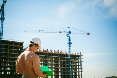 Genç seksi erkek vücut geliştirmeci atlet. Müdür mühendis Oluşturucu koruyucu kask yapı ve inşaat İnşaat arka plan üzerinde duran beyaz belgeleri ile el vinç