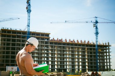 Çıplak bir gövde ile genç seksi erkek vücut geliştirmeci atlet. İnşaat yapı ve inşaat vinç belgeler ile arka plan üzerinde beyaz koruyucu kask Yöneticisi mühendis Oluşturucu standları