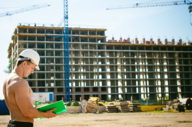 Çıplak bir gövde ile genç seksi erkek vücut geliştirmeci atlet. İnşaat yapı ve inşaat vinç belgeler ile arka plan üzerinde beyaz koruyucu kask Yöneticisi mühendis Oluşturucu standları