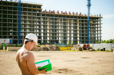 Çıplak bir gövde ile genç seksi erkek vücut geliştirmeci atlet. İnşaat yapı ve inşaat vinç belgeler ile arka plan üzerinde beyaz koruyucu kask Yöneticisi mühendis Oluşturucu standları